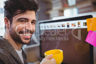 Handsome businessman holding coffee cup by computer