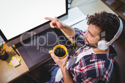 Businessman pointing at computer monitor while drinking coffee