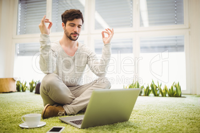 Businessman doing yoga in front of laptop in office