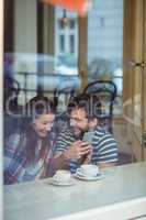 Cheerful couple using cellphone at cafe