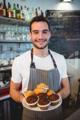 Portrait of confident waiter with cupcakes at cafe