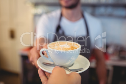 Cropped image of customer taking coffee from waiter at cafe
