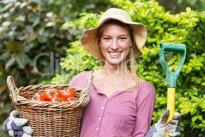 Female gardener holding tomato basket and work tool