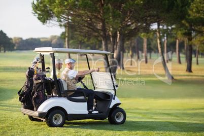 Mature golfer friends sitting in golf buggy