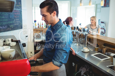 Waiter working while barista talking with customer at cafeteria