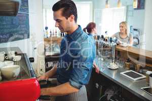 Waiter working while barista talking with customer at cafeteria