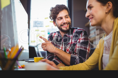 Businessman pointing at computer while colleague in foreground