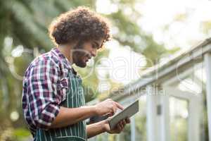 Male gardener using tablet computer outside greenhouse