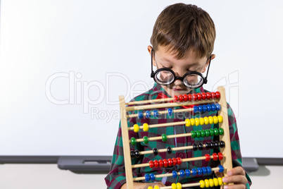Cute boy playing with abacus in classroom