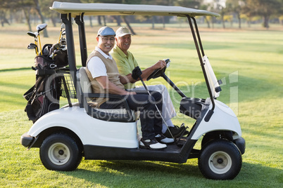 Happy male golfer friends sitting in golf buggy