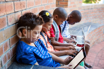 Students using dital tablet and laptop at school corridor