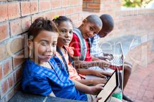 Portrait of students using digital tablet and laptop at corridor