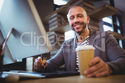 Creative businessman holding disposable cup while using graphics