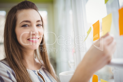Portrait of businesswoman holding adhesive notes on window in cr