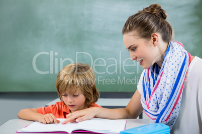 Teacher assisting boy reading book in classroom