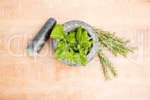 Mortar and pestle with basil and rosemary on table