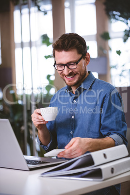 Happy businessman drinking coffee looking at mobile phone in cre