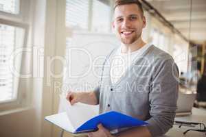 Portrait of businessman holding file at creative office