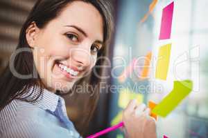 Creative businesswoman writing on sticky notes stuck to glass