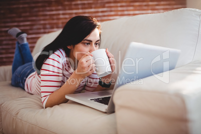 Woman drinking coffee while lying on couch