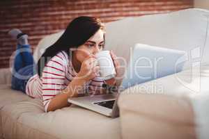 Woman drinking coffee while lying on couch