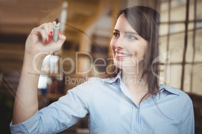Businesswoman smiling while writing on glass with marker pen