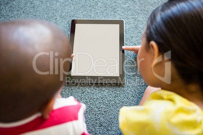 Siblings using digital tablet on carpet