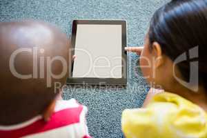 Siblings using digital tablet on carpet
