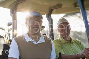 Smiling golfer friends sitting in golf buggy