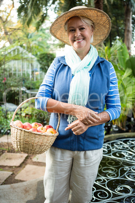 Portrait of happy woman standing with apples at garden