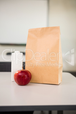 Apple with drink bottle and paper bag on table in classroom