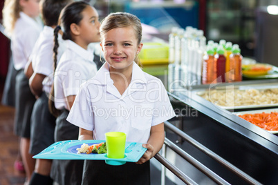 Cute schoolgirl with classmate standing near canteen counter