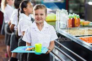 Cute schoolgirl with classmate standing near canteen counter