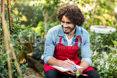 Smiling male gardener writing on clipboard