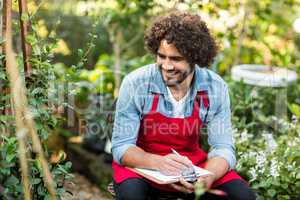 Smiling male gardener writing on clipboard