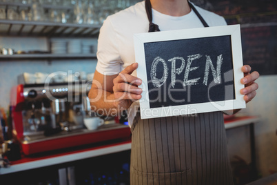 Midsection of waiter holding chalkboard at cafe