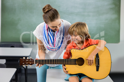 Teacher assisting boy to play guitar