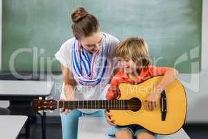 Teacher assisting boy to play guitar