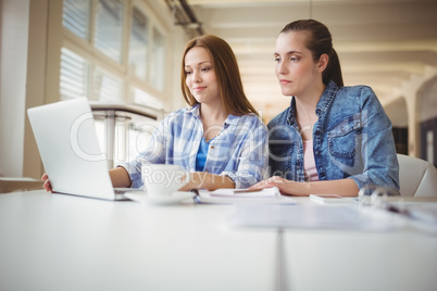 Female colleagues working on laptop at desk in creative office