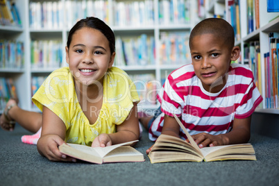 Portrait of students reading books while lying at library