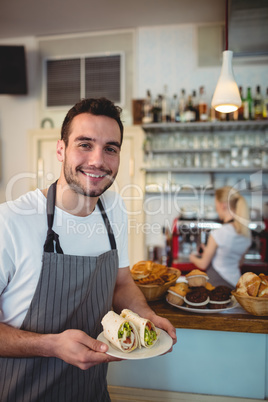 Portrait of happy waiter with fresh rolls at cafe