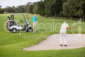 Mature golfer standing on sand trap by woman