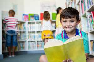 Portrait of boy holding book at school library