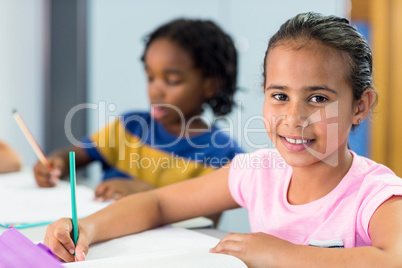 Smiling schoolgirl with classmate writing on book