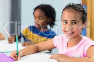 Smiling schoolgirl with classmate writing on book