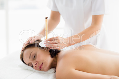 Woman receiving ear candle treatment from masseur
