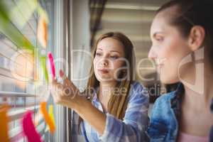 Businesswoman sticking adhesive notes on window in office