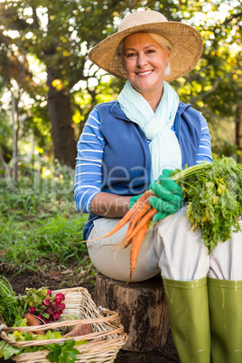 Portrait of happy gardener with carrots sitting at garden