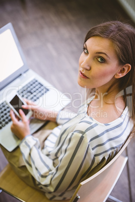 Portrait of confident businesswoman using cellphone over laptop
