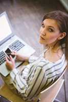 Portrait of confident businesswoman using cellphone over laptop